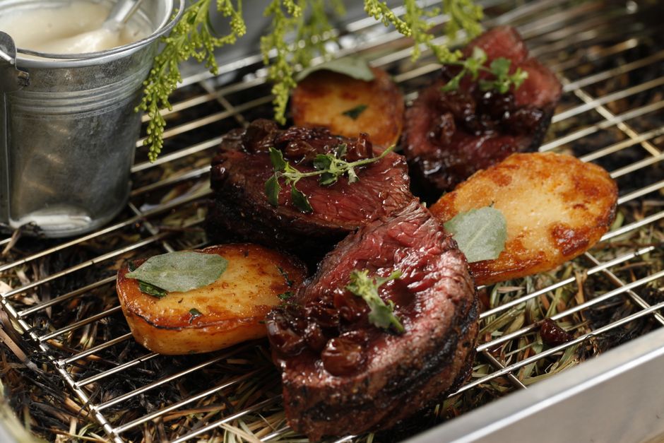 Delicious grilled steak and roasted potatoes garnished with herbs on a metal rack.